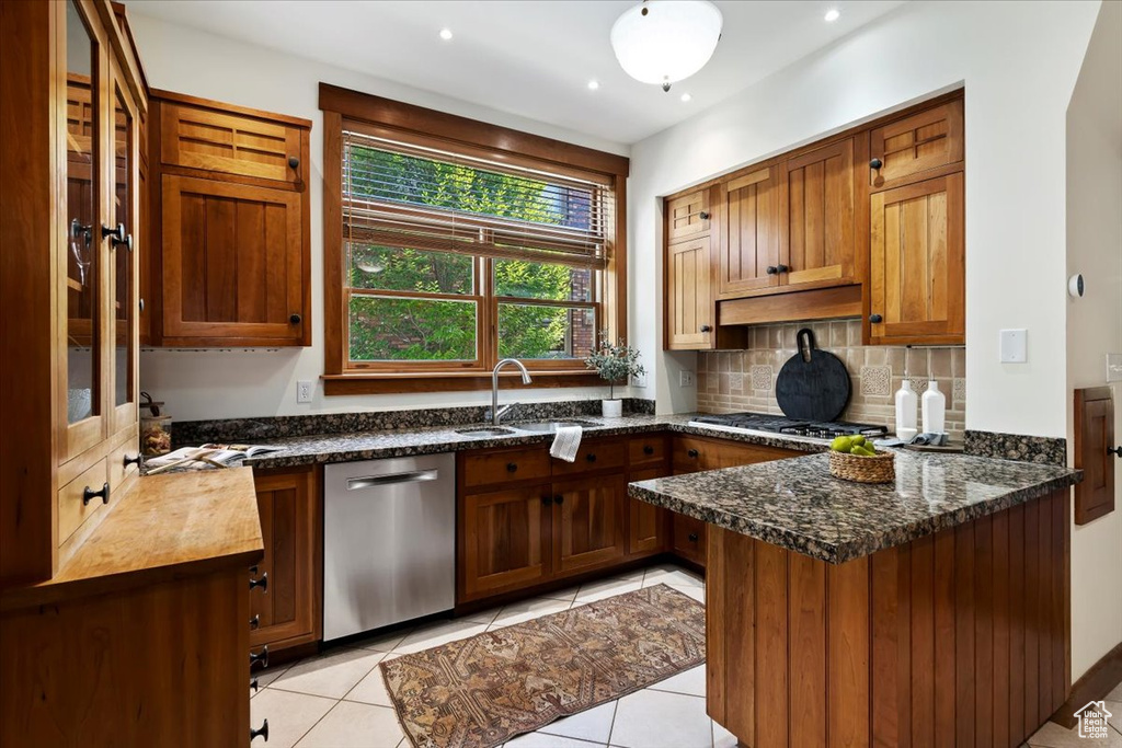 Kitchen featuring appliances with stainless steel finishes, light tile patterned floors, dark stone counters, and kitchen peninsula