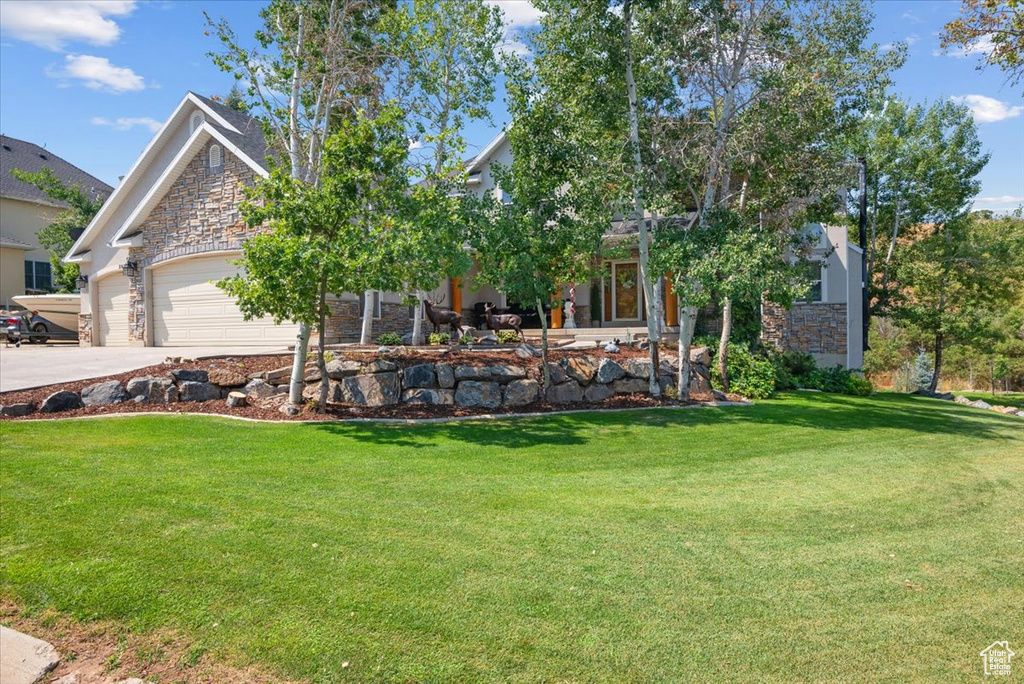 View of property hidden behind natural elements featuring a garage and a front lawn