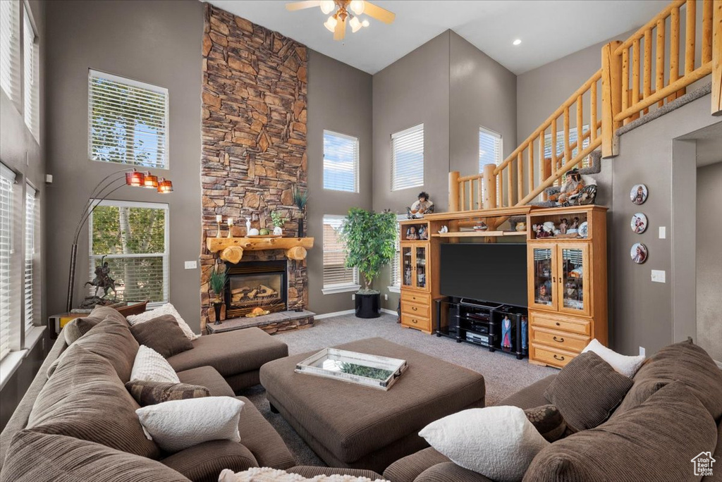 Living room with a stone fireplace, a towering ceiling, carpet floors, and ceiling fan