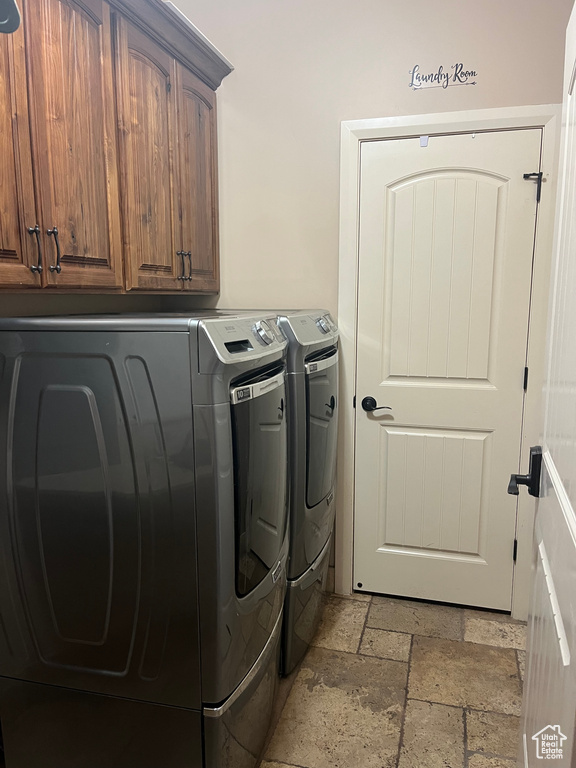 Clothes washing area featuring separate washer and dryer, cabinet space, and stone tile floors