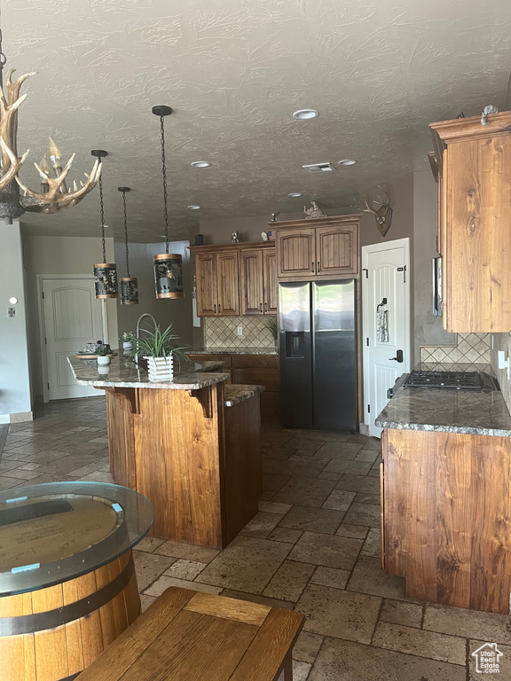 Kitchen featuring brown cabinetry, tasteful backsplash, a breakfast bar, a kitchen island with sink, and stainless steel fridge