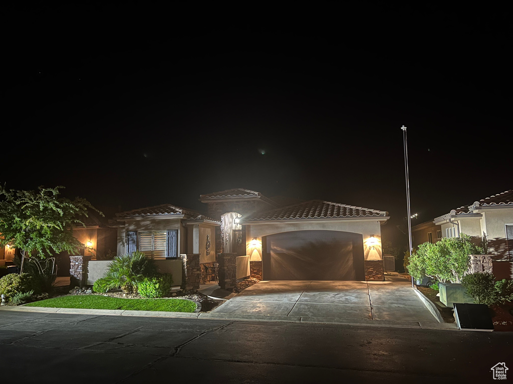 View of front of house featuring an attached garage, driveway, a tile roof, and stucco siding