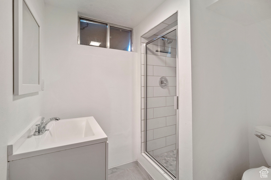 Bathroom featuring a shower with door, vanity, tile patterned floors, and toilet