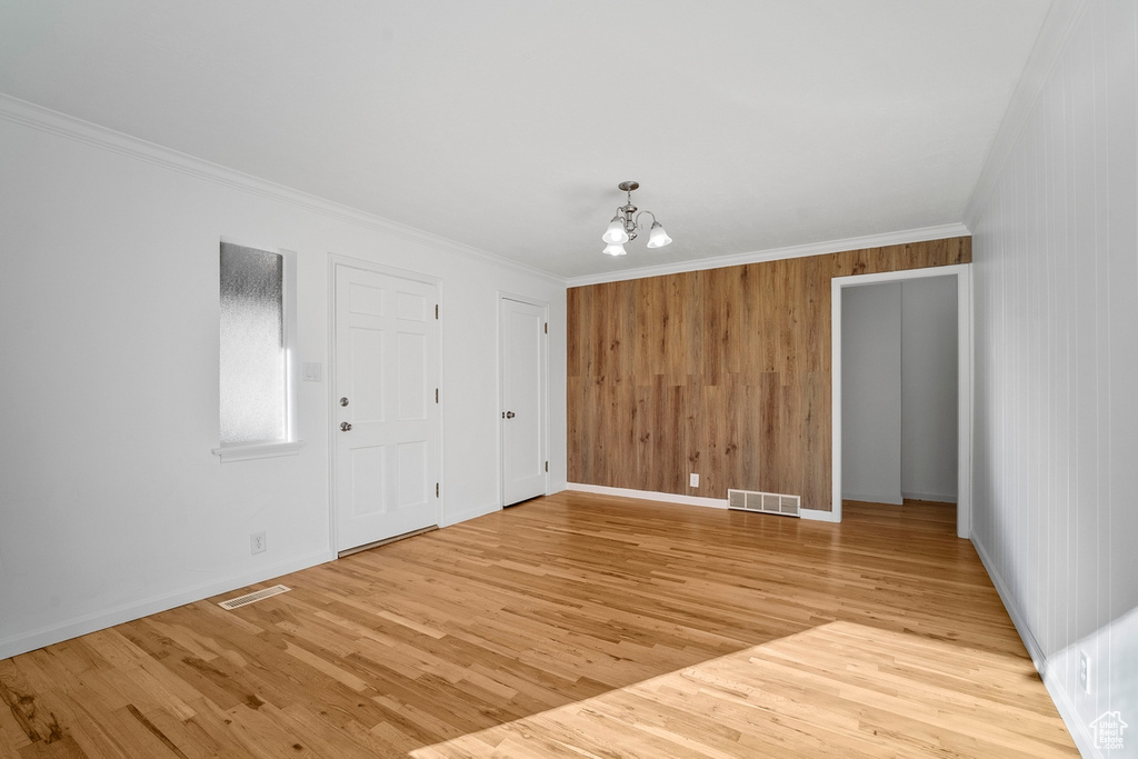 Unfurnished room with a notable chandelier, crown molding, and light wood-type flooring