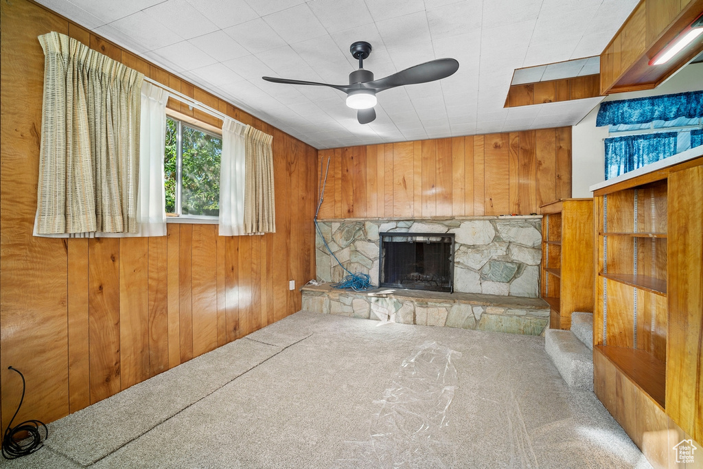 Unfurnished living room with carpet floors, wood walls, a fireplace, and ceiling fan