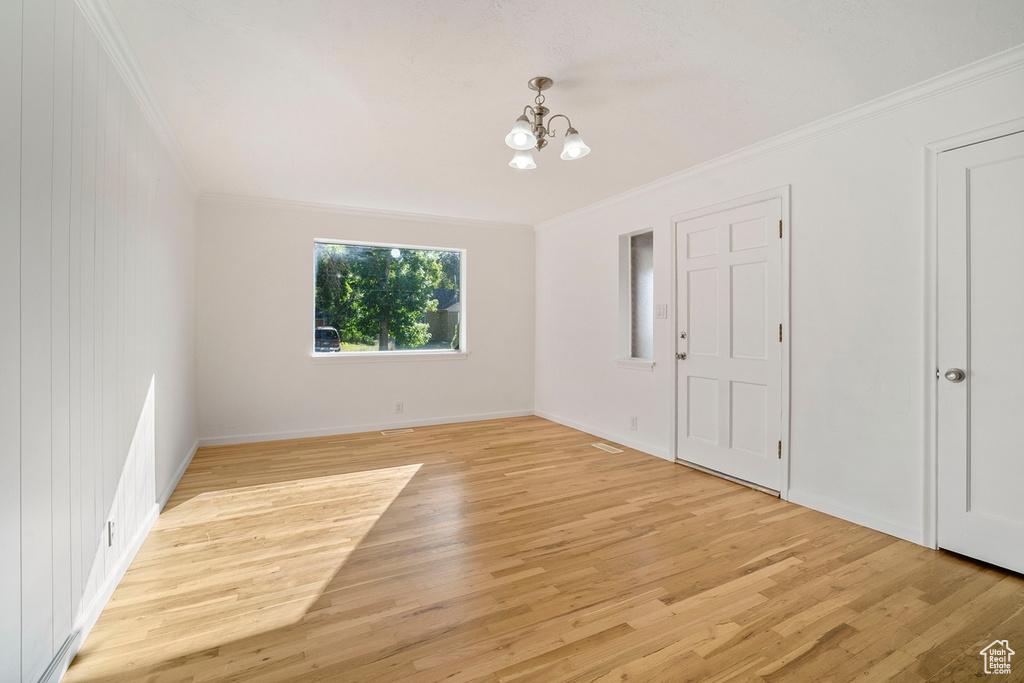 Empty room featuring an inviting chandelier, light hardwood / wood-style flooring, and ornamental molding