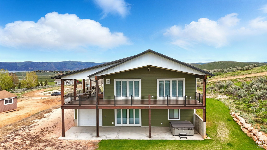 Rear view of property featuring a hot tub, a mountain view, a patio area, and a garage