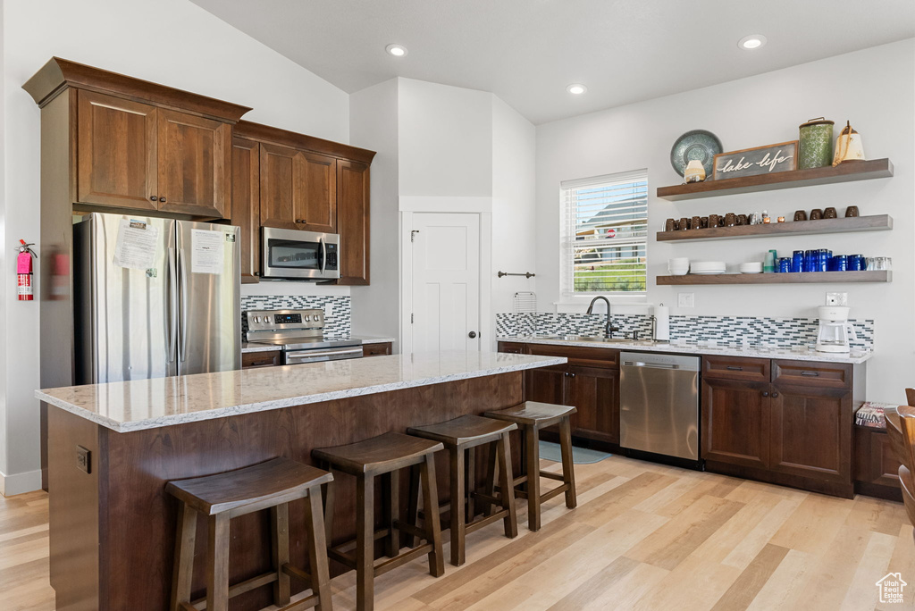 Kitchen featuring light hardwood / wood-style floors, appliances with stainless steel finishes, a center island, and backsplash