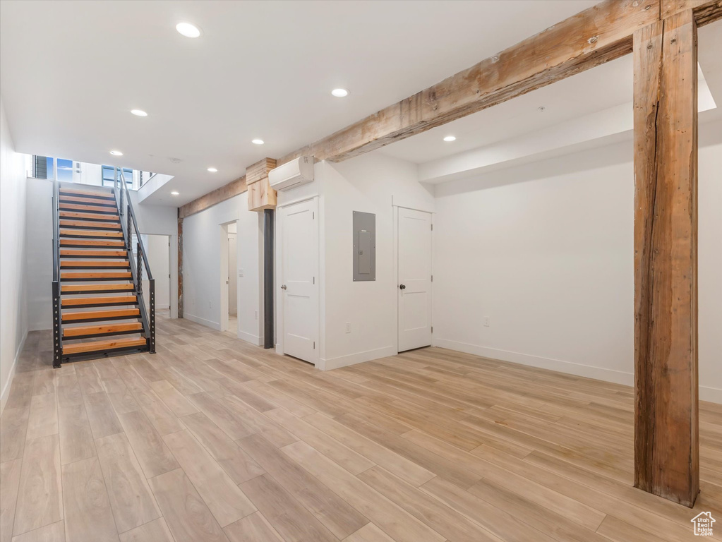 Basement with a wall mounted AC, light hardwood / wood-style floors, and electric panel