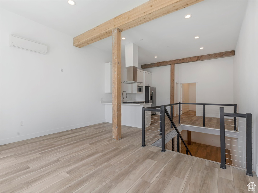 Interior space featuring sink, an AC wall unit, beamed ceiling, and light wood-type flooring