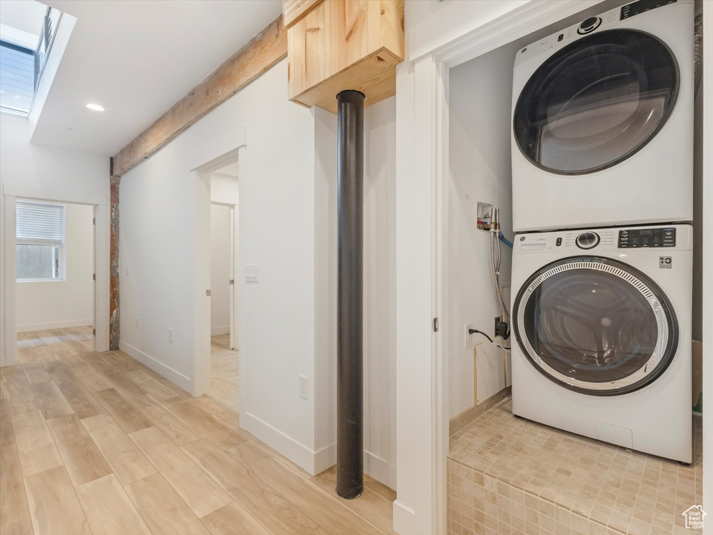 Laundry room with a skylight, light hardwood / wood-style flooring, and stacked washer / drying machine