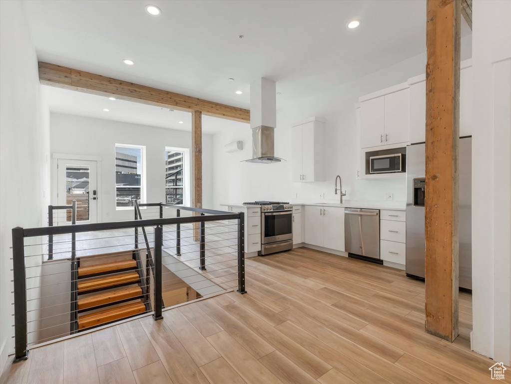 Kitchen featuring stainless steel appliances, white cabinets, wall chimney exhaust hood, beam ceiling, and light hardwood / wood-style floors