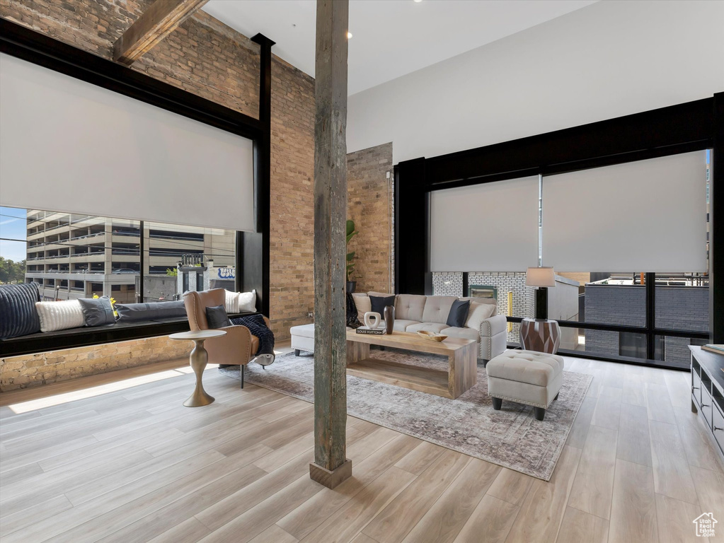 Living room featuring brick wall, light hardwood / wood-style floors, and a towering ceiling