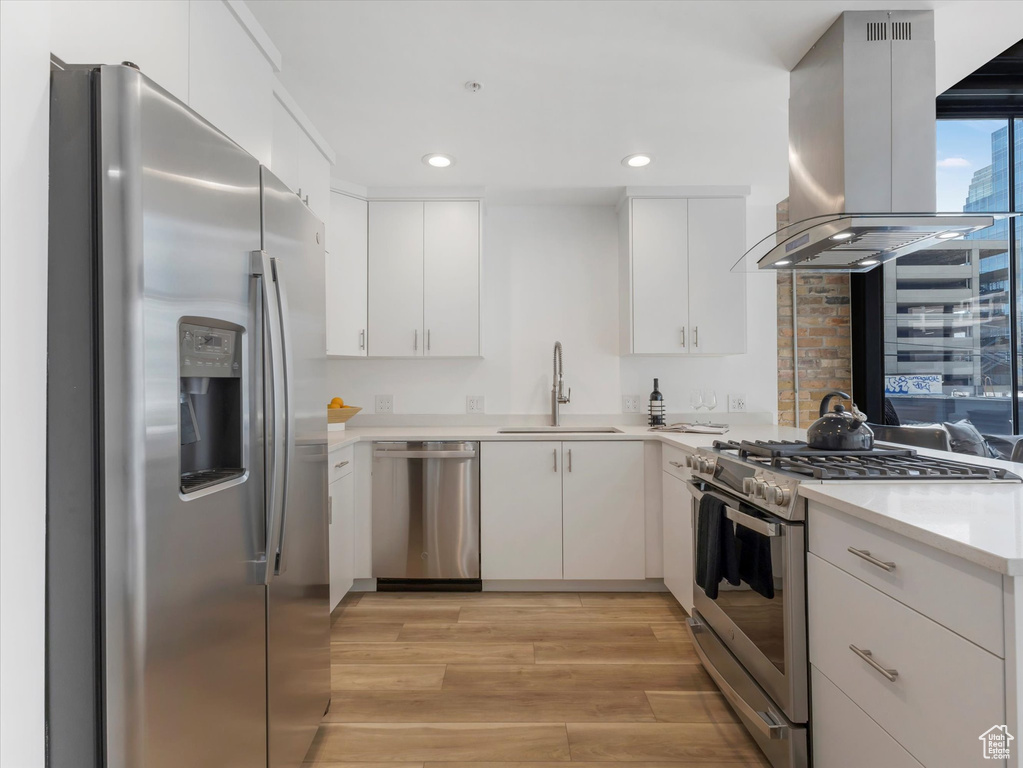 Kitchen with stainless steel appliances, white cabinets, island exhaust hood, sink, and light hardwood / wood-style floors