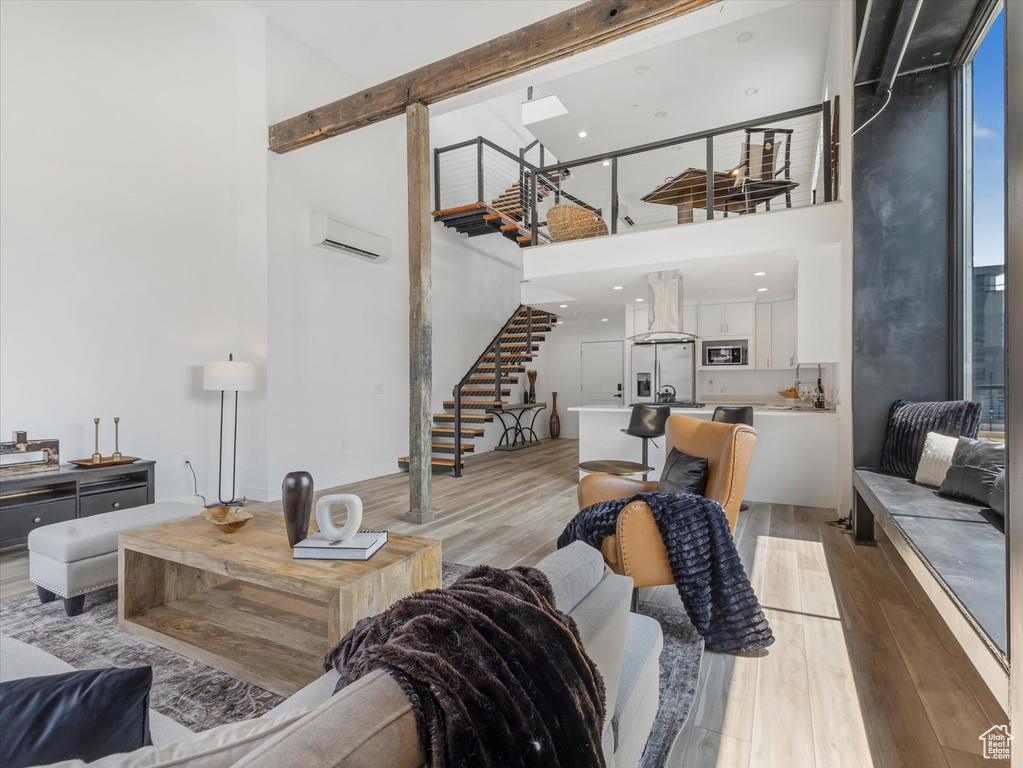 Living room with light hardwood / wood-style floors, a wall unit AC, and a high ceiling