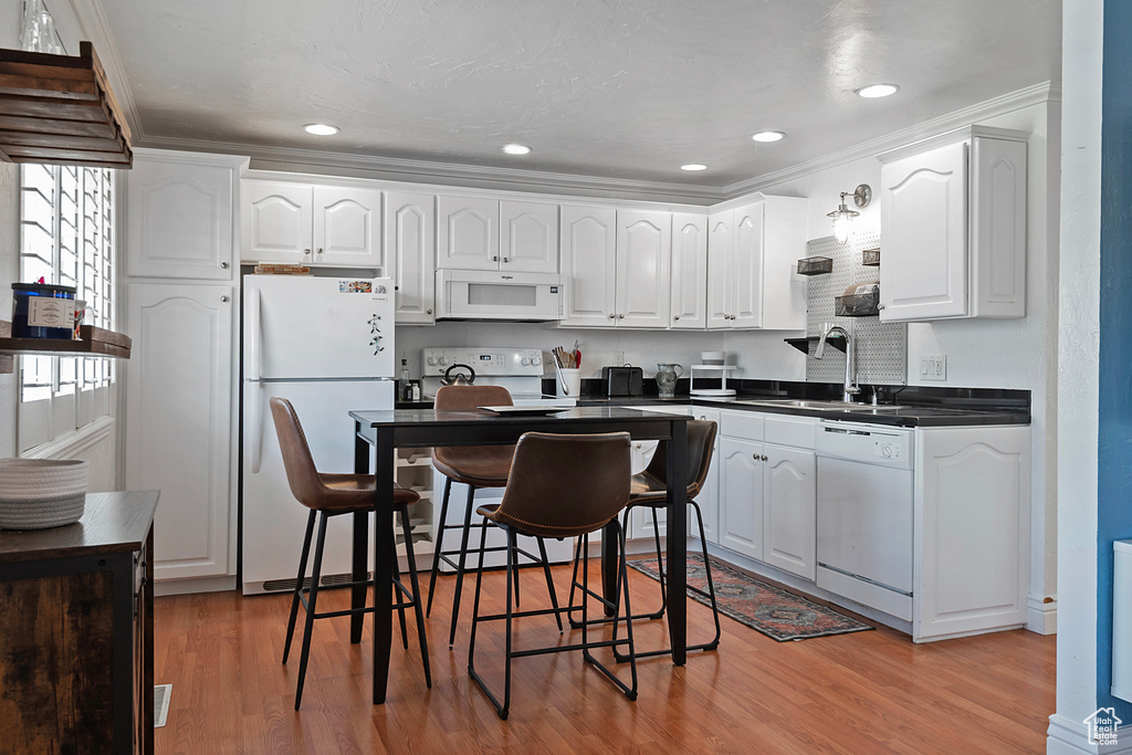 Kitchen with white cabinetry, light hardwood / wood-style flooring, and white appliances