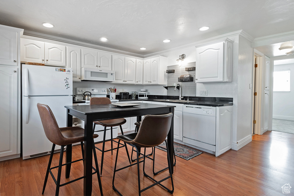 Kitchen featuring white cabinetry, light hardwood / wood-style flooring, white appliances, sink, and ornamental molding