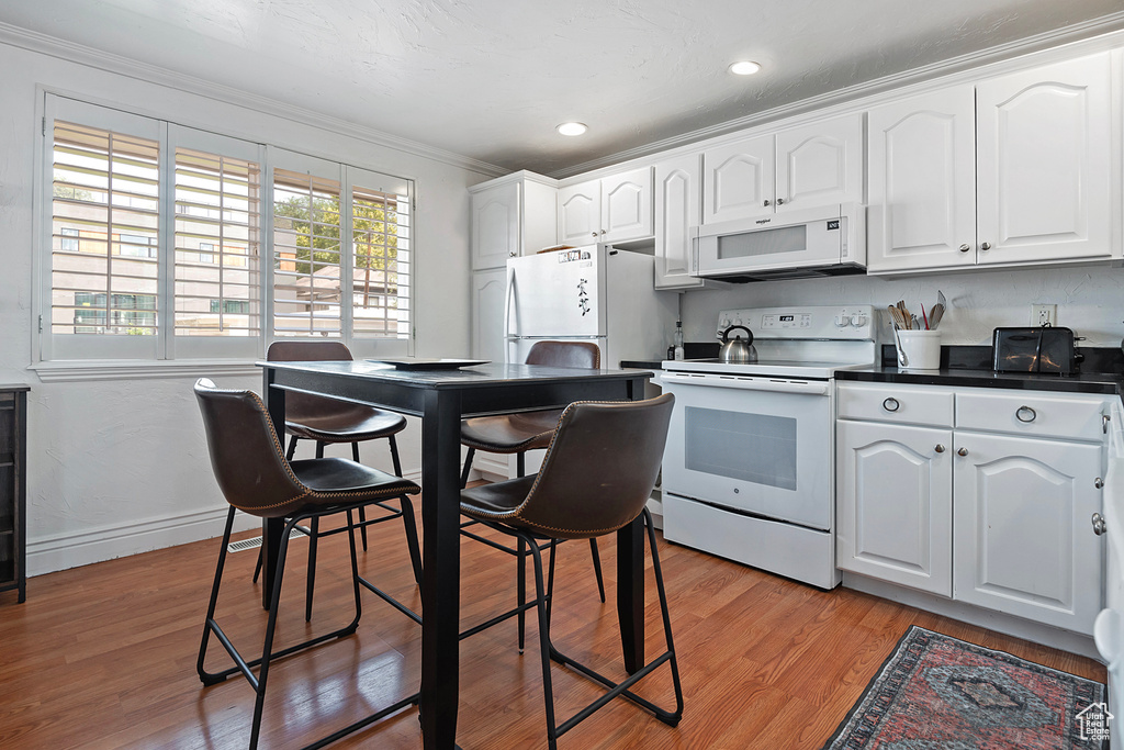 Kitchen featuring white cabinets, crown molding, light wood-type flooring, and white appliances