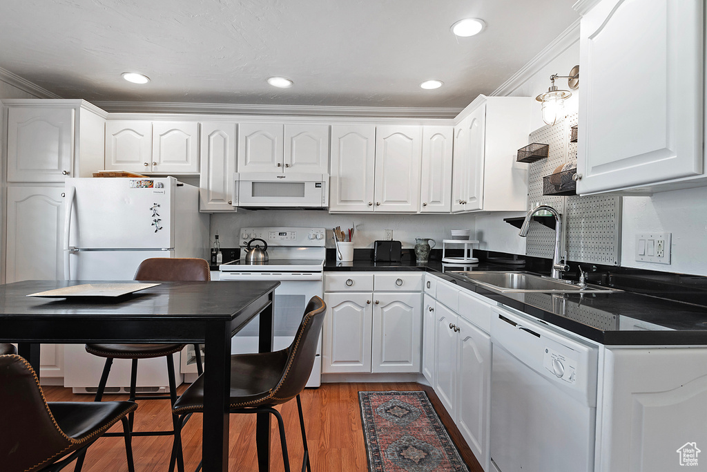 Kitchen with white appliances, sink, crown molding, light wood-type flooring, and white cabinetry