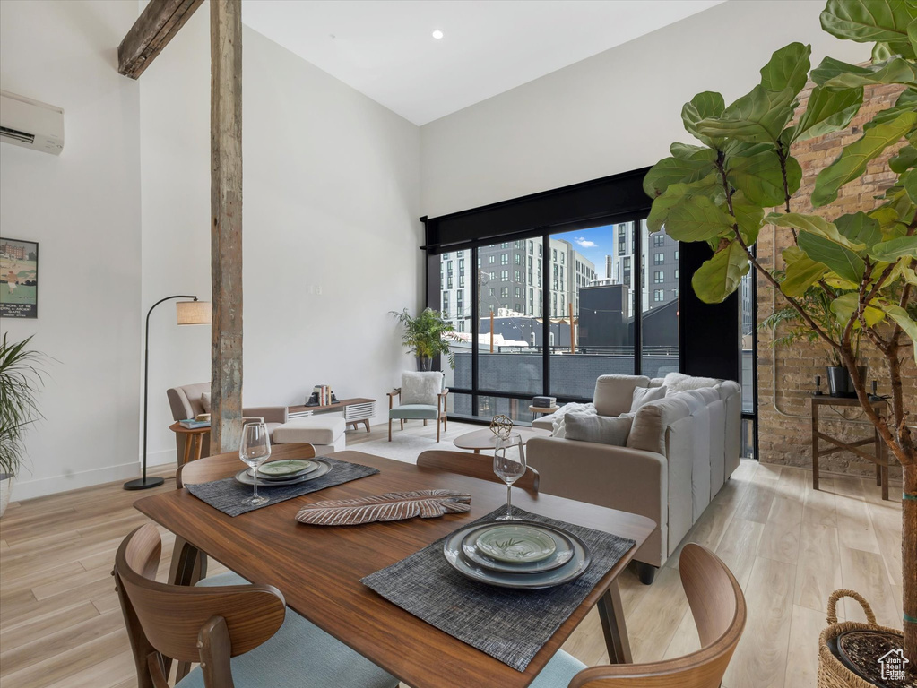 Dining room with a wall unit AC, light hardwood / wood-style flooring, and a towering ceiling