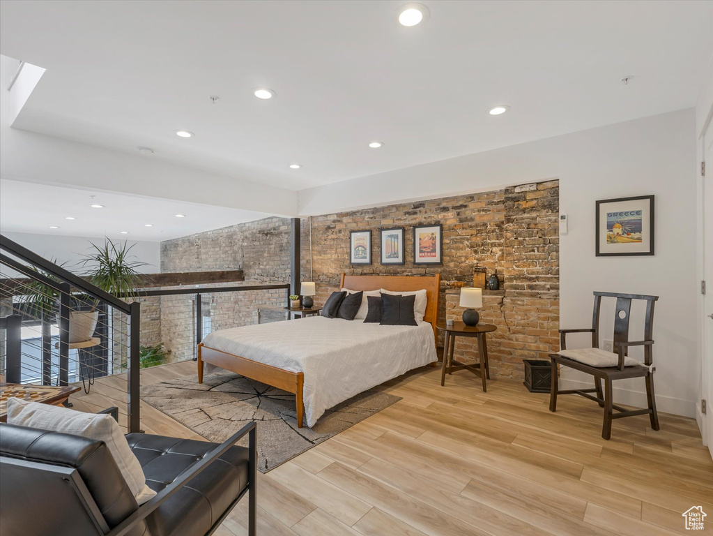 Bedroom featuring a skylight, multiple windows, brick wall, and light wood-type flooring