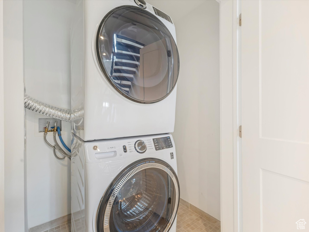 Clothes washing area featuring light tile patterned flooring and stacked washer and dryer