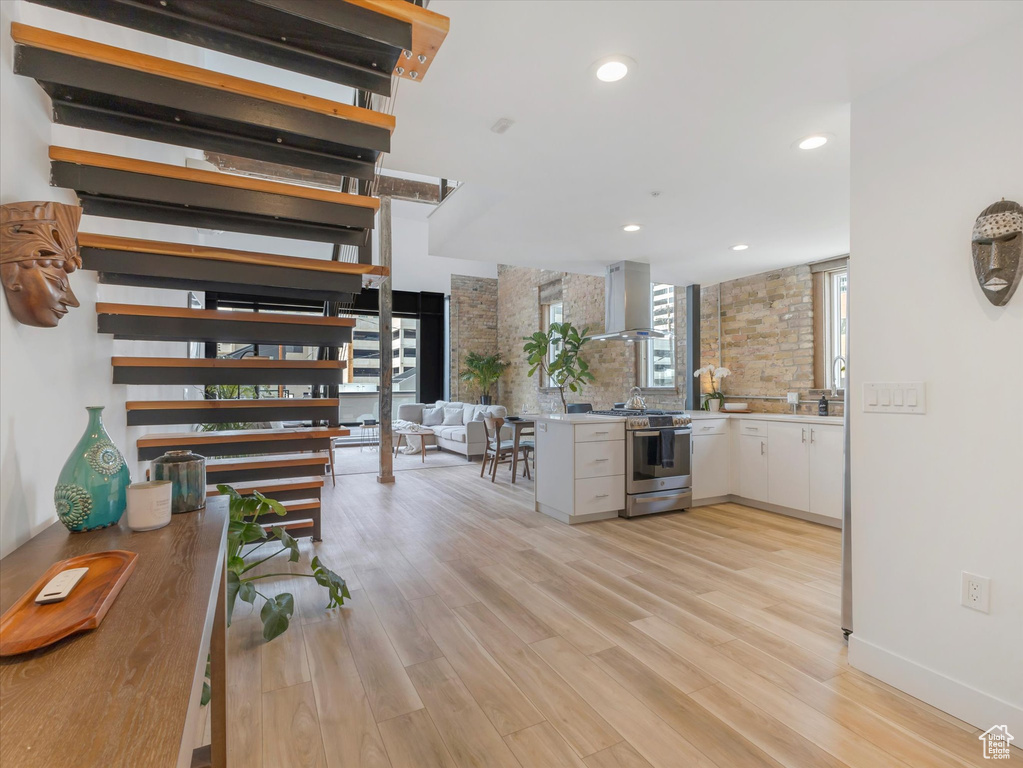 Kitchen featuring white cabinetry, light hardwood / wood-style flooring, tasteful backsplash, stainless steel range with gas cooktop, and wall chimney exhaust hood