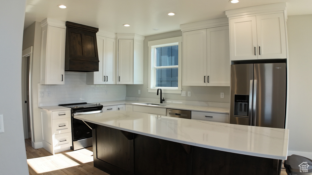 Kitchen featuring appliances with stainless steel finishes, sink, premium range hood, light wood-type flooring, and a center island