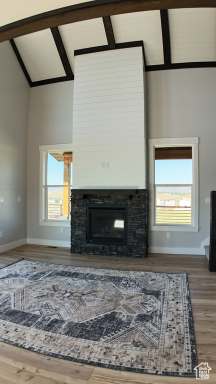 Unfurnished living room featuring hardwood / wood-style flooring, beamed ceiling, a wealth of natural light, and high vaulted ceiling