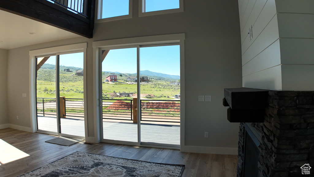 Doorway to outside with a mountain view, light hardwood / wood-style flooring, a stone fireplace, and a high ceiling