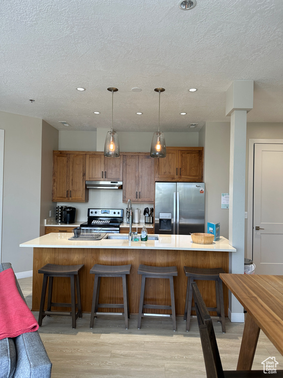 Kitchen featuring a breakfast bar area, light wood-type flooring, stainless steel appliances, pendant lighting, and a large island with sink