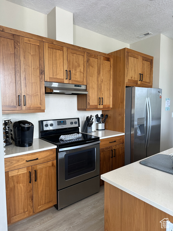 Kitchen featuring stainless steel appliances, light wood-type flooring, and a textured ceiling