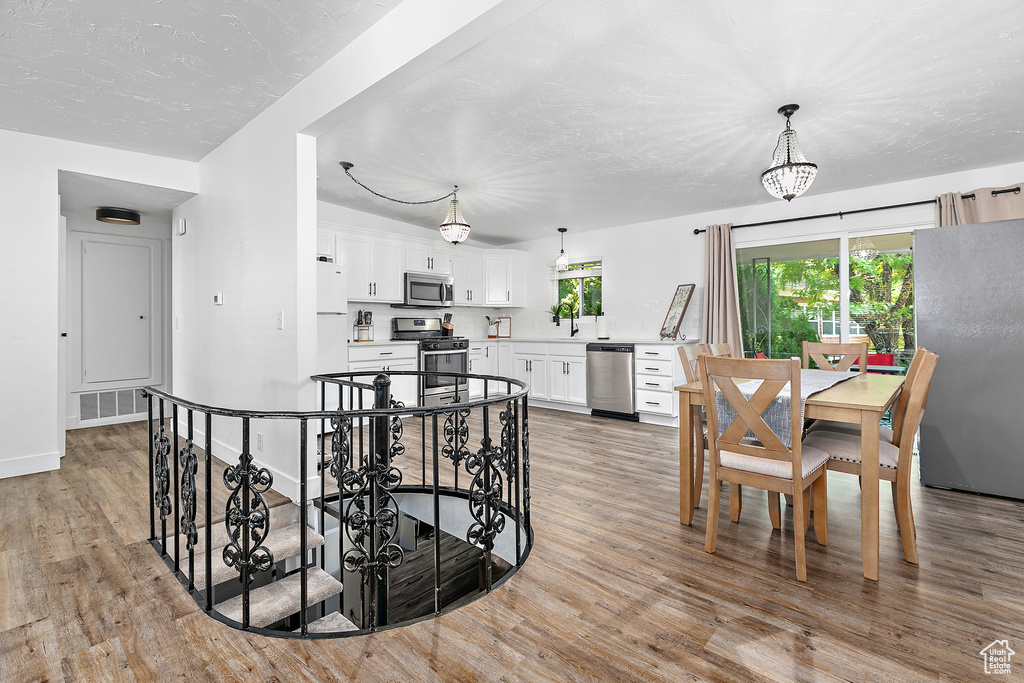 Interior space with white cabinetry, light wood-type flooring, hanging light fixtures, and stainless steel appliances