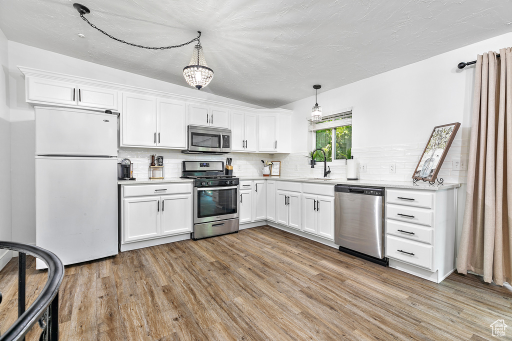 Kitchen featuring light hardwood / wood-style flooring, white cabinets, stainless steel appliances, hanging light fixtures, and decorative backsplash