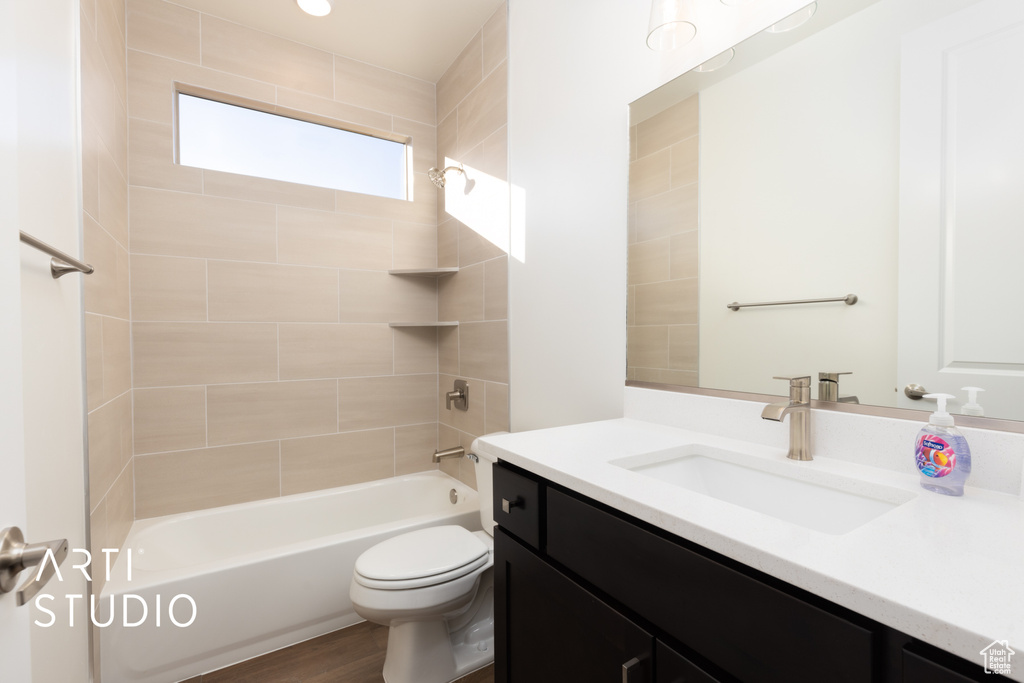 Full bathroom with vanity, tiled shower / bath combo, hardwood / wood-style flooring, and toilet