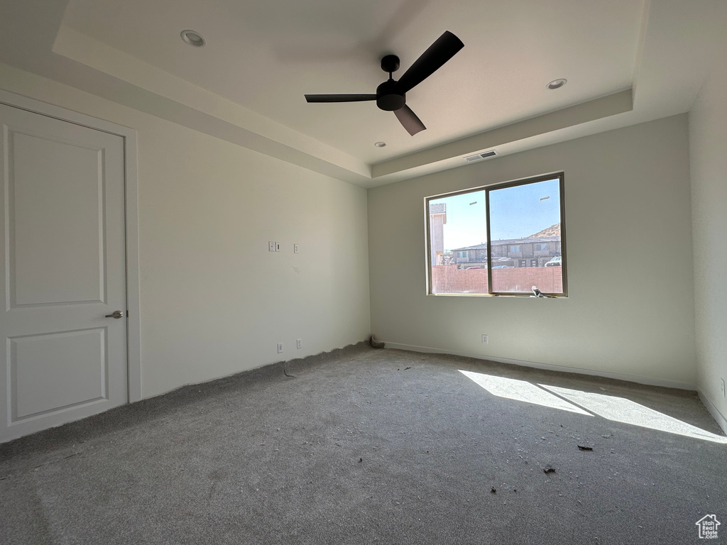 Carpeted spare room featuring ceiling fan and a tray ceiling