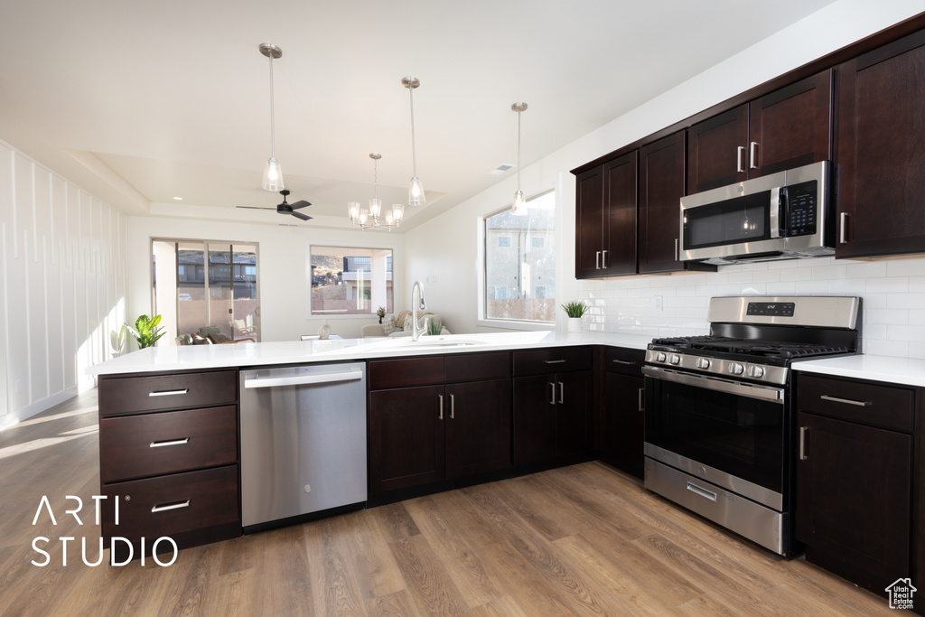 Kitchen with kitchen peninsula, hardwood / wood-style floors, dark brown cabinets, appliances with stainless steel finishes, and sink