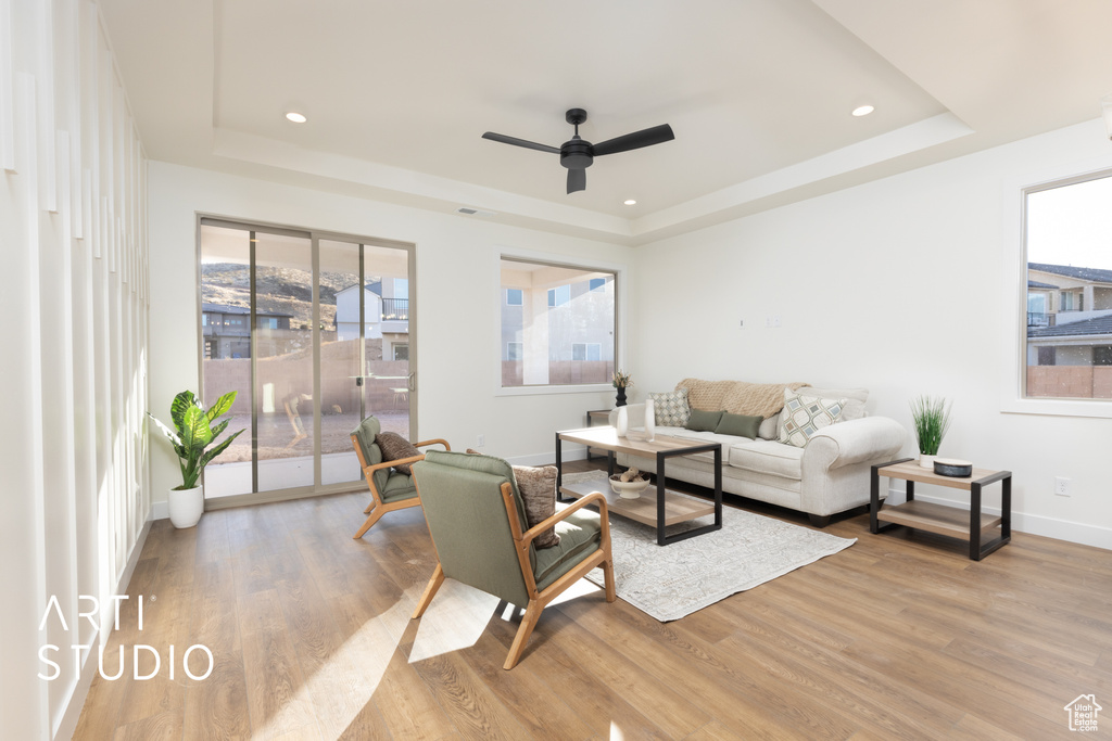 Living room featuring light hardwood / wood-style flooring, ceiling fan, and a raised ceiling