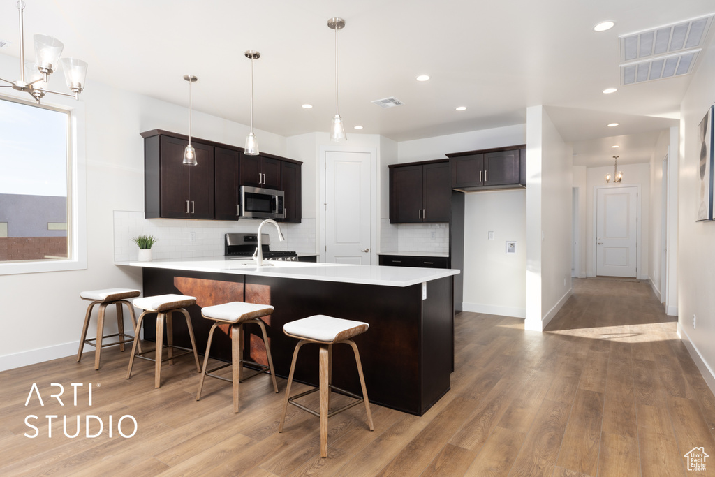 Kitchen with kitchen peninsula, stainless steel appliances, a kitchen bar, pendant lighting, and light wood-type flooring