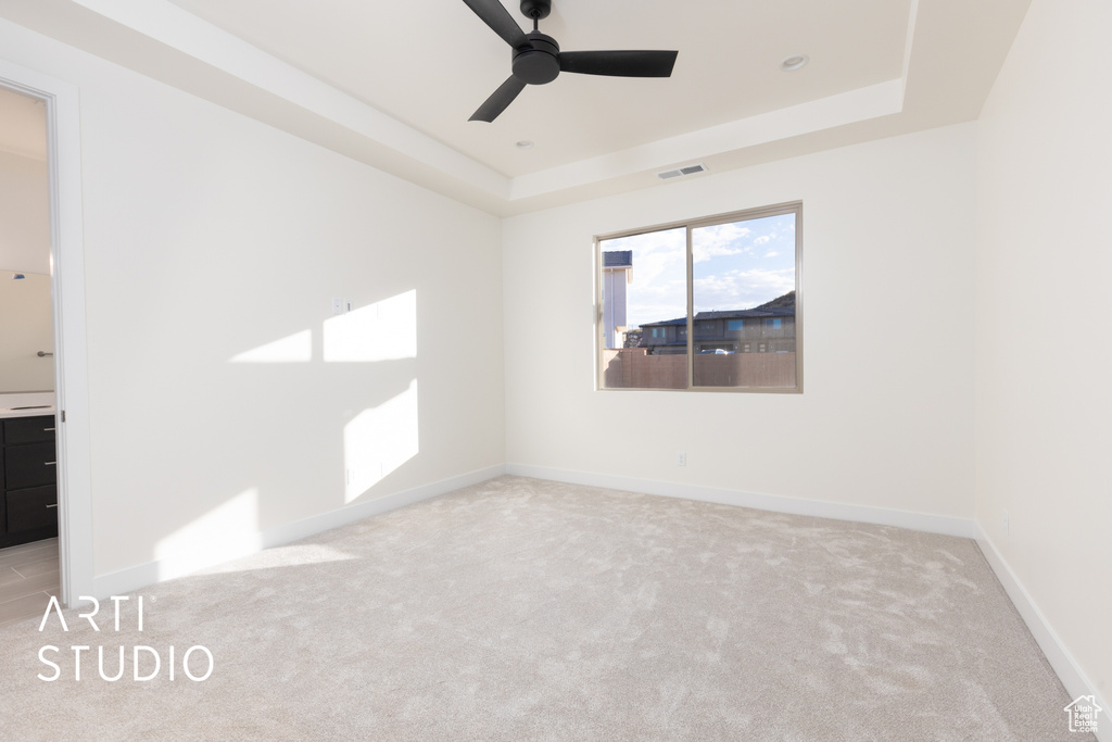 Carpeted spare room featuring ceiling fan and a raised ceiling