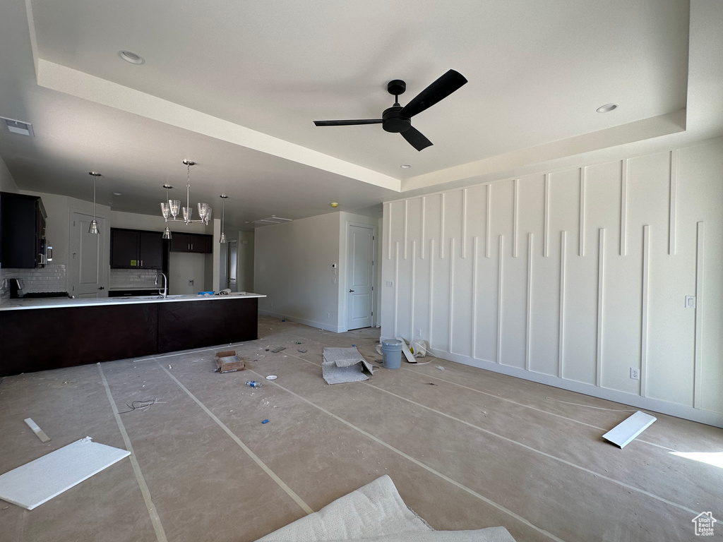 Unfurnished living room featuring ceiling fan with notable chandelier, a tray ceiling, and sink