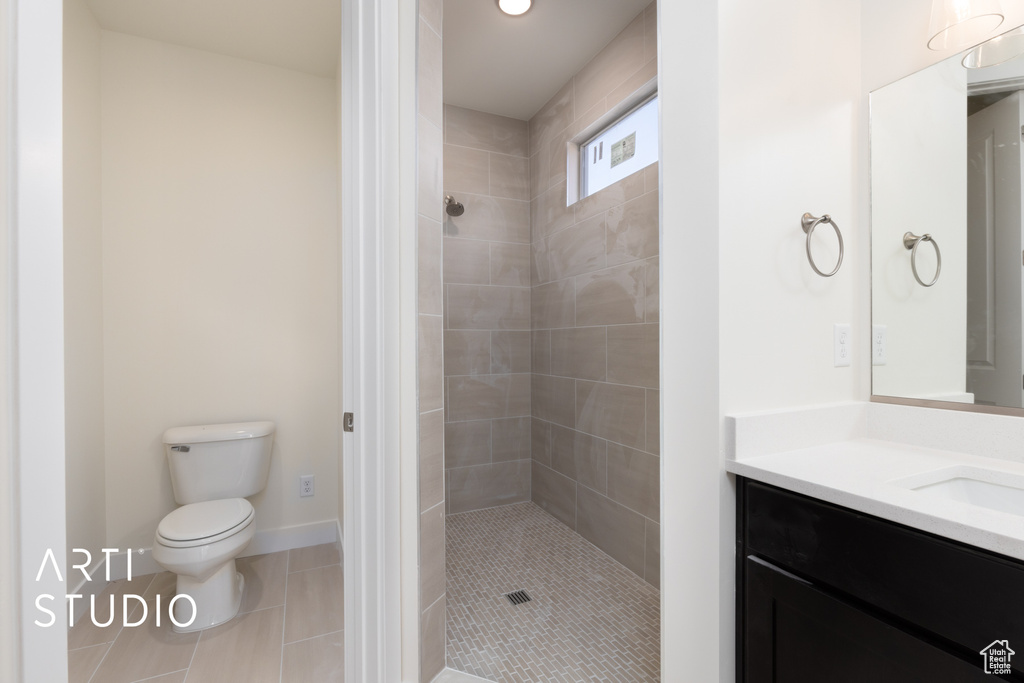 Bathroom with vanity, toilet, tile patterned floors, and tiled shower