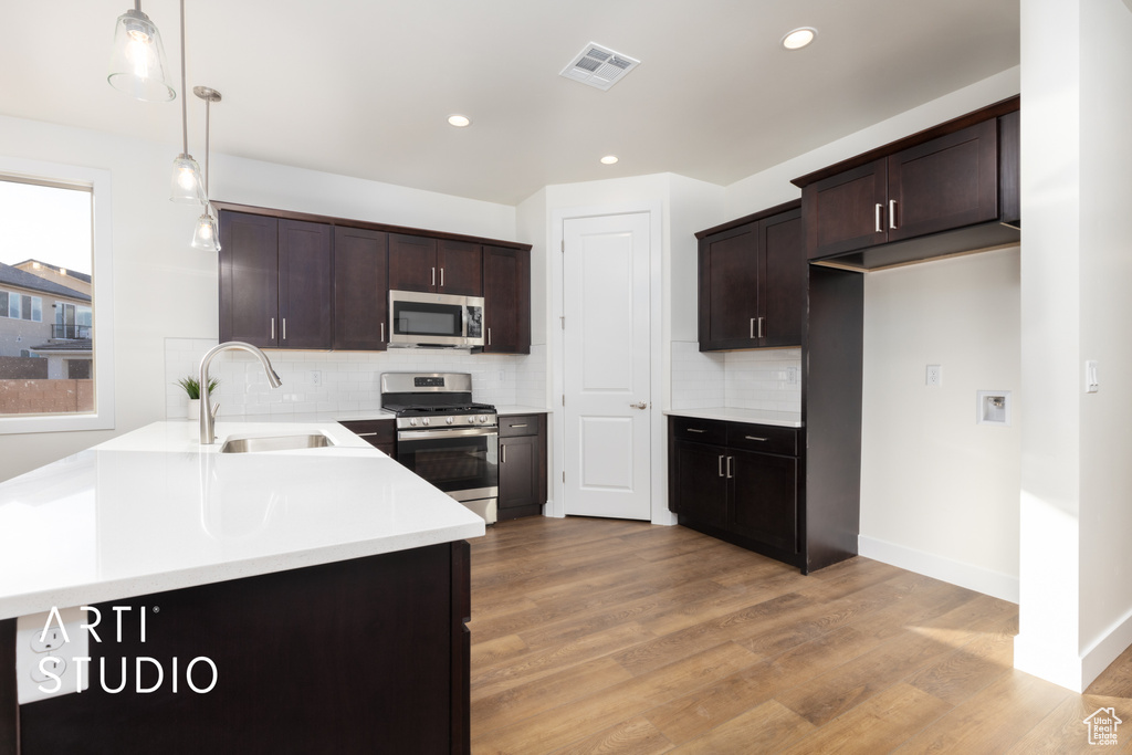 Kitchen featuring appliances with stainless steel finishes, light hardwood / wood-style flooring, pendant lighting, dark brown cabinetry, and sink