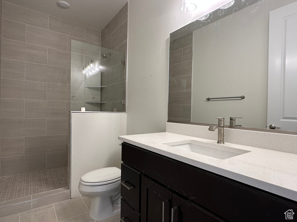 Bathroom featuring tile patterned floors, tiled shower, toilet, and vanity