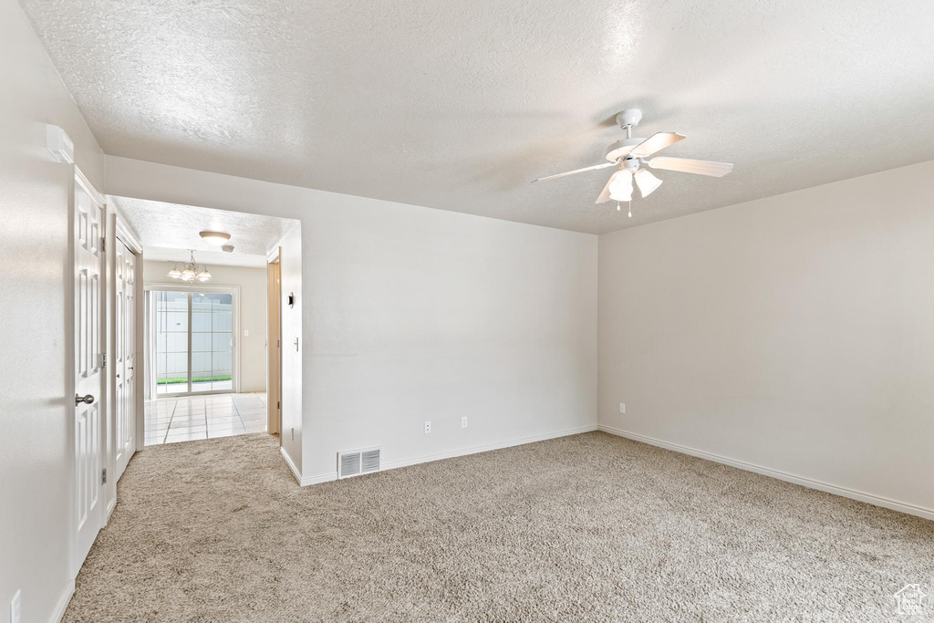 Carpeted spare room with a textured ceiling and ceiling fan with notable chandelier