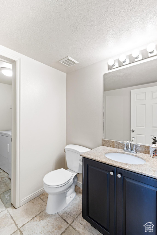 Bathroom featuring a textured ceiling, toilet, vanity, tile patterned floors, and washer / dryer