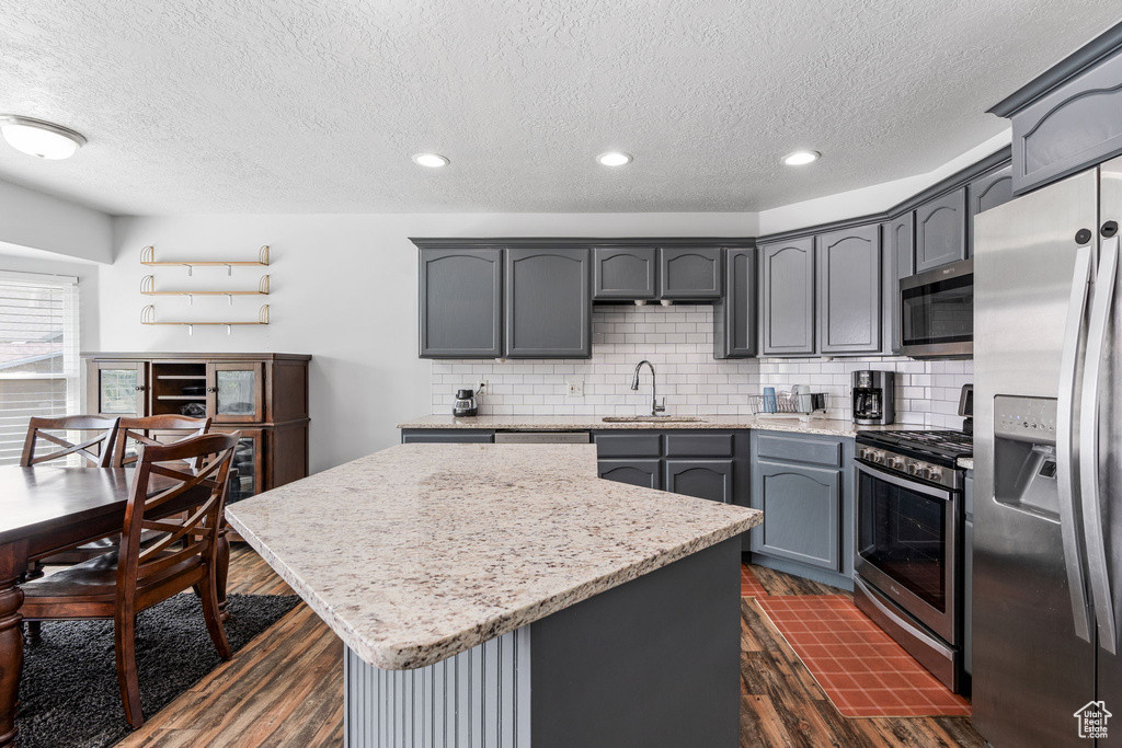 Kitchen with decorative backsplash, dark hardwood / wood-style floors, appliances with stainless steel finishes, and gray cabinetry