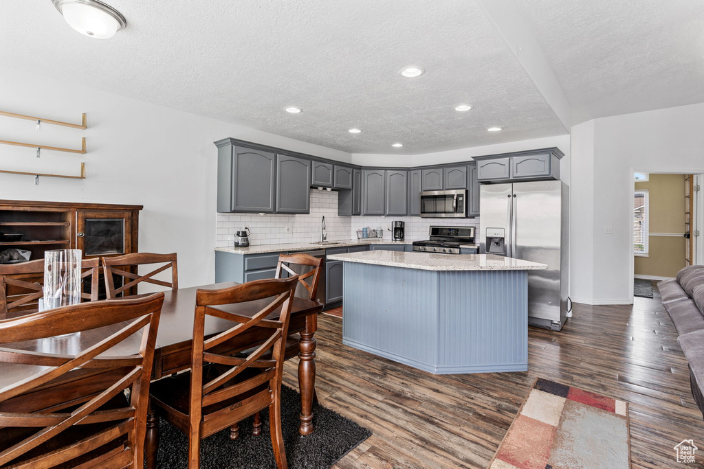 Kitchen with stainless steel appliances, gray cabinetry, a kitchen island, and dark wood-type flooring