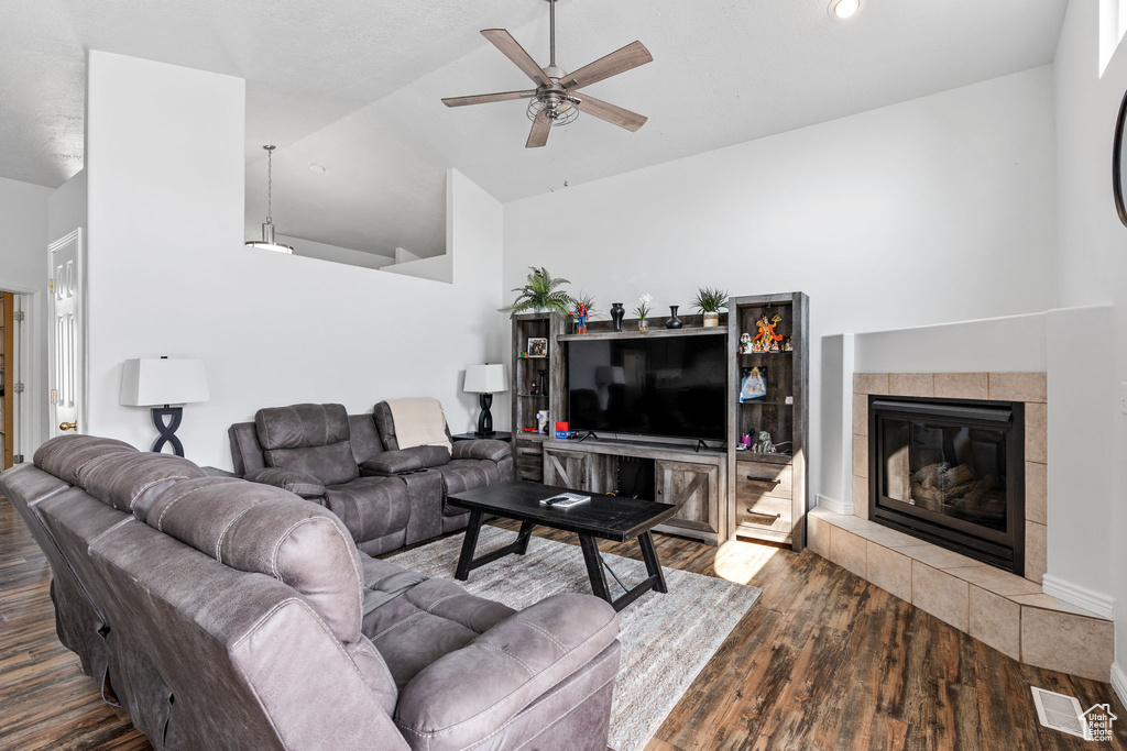 Living room with a fireplace, dark wood-type flooring, ceiling fan, and high vaulted ceiling