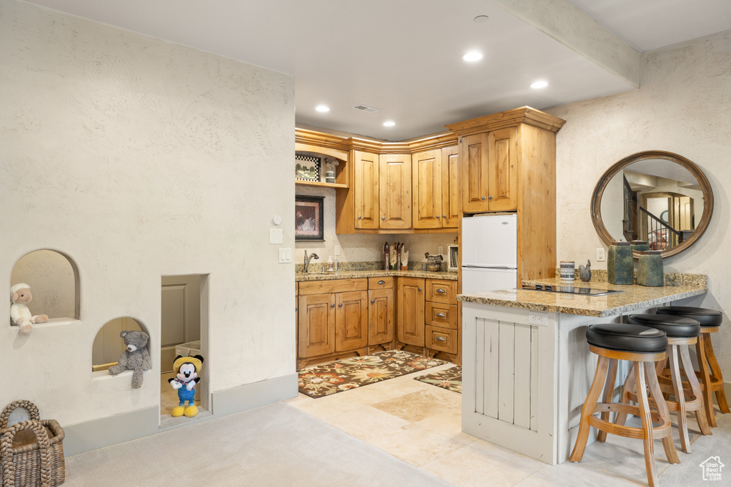 Kitchen featuring a breakfast bar area, sink, kitchen peninsula, light tile patterned floors, and white fridge